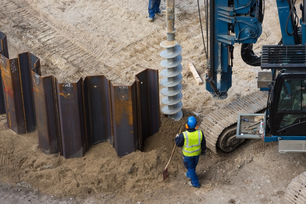 Ouvrier sur un chantier utilisant des palplanches métalliques et une foreuse pour des travaux de terrassement